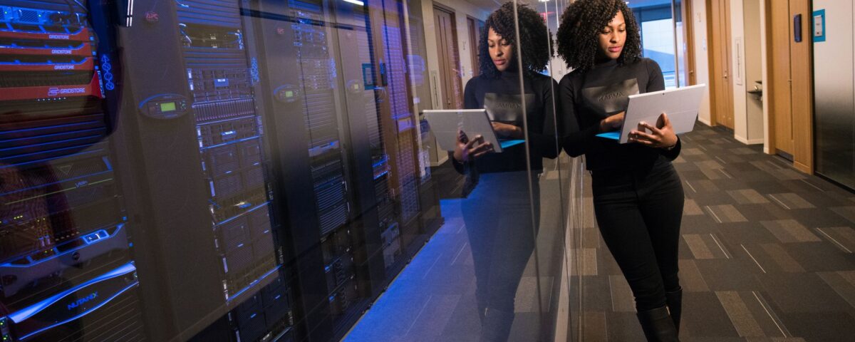 A woman using a laptop navigating a contemporary data center with mirrored servers.