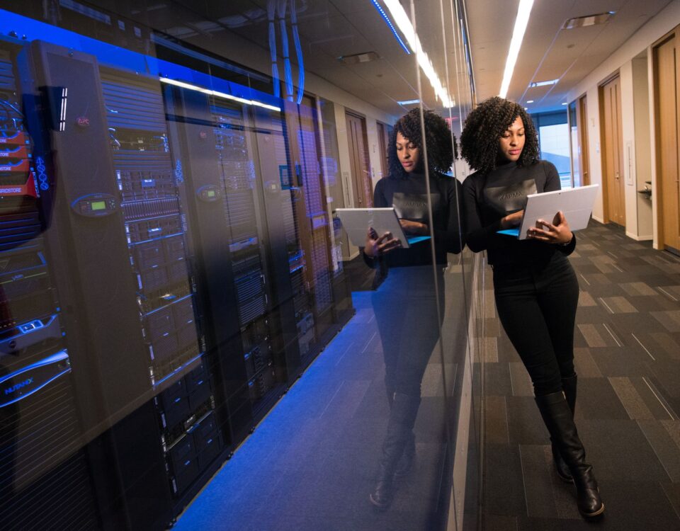 A woman using a laptop navigating a contemporary data center with mirrored servers.