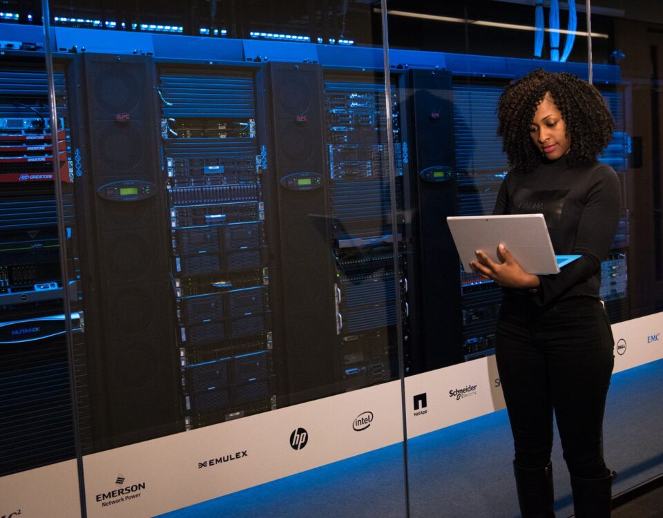 A female engineer using a laptop while monitoring data servers in a modern server room.