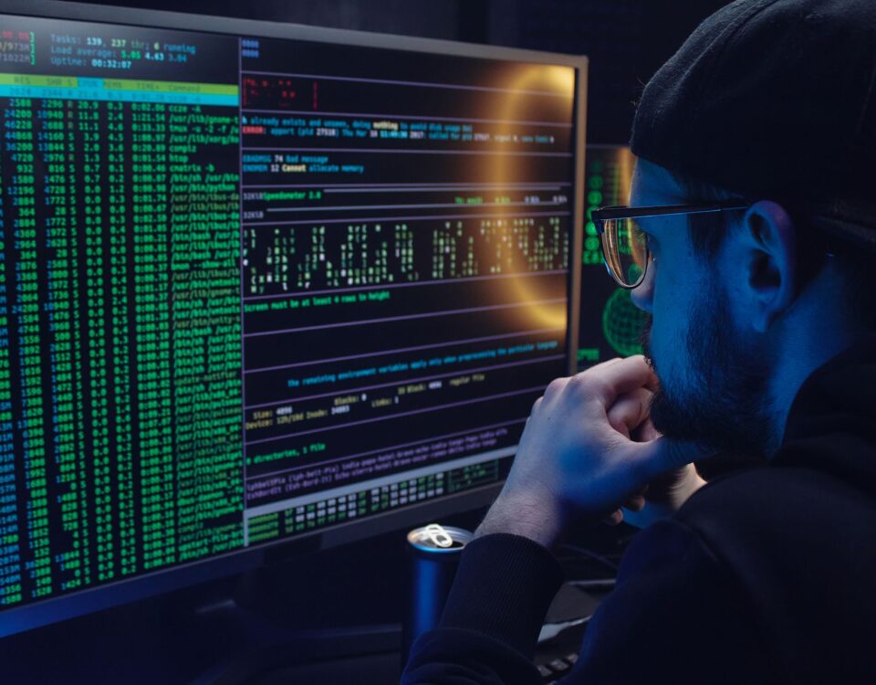 Man intently working on computer programming with code displayed on dual monitors in a dimly lit room.