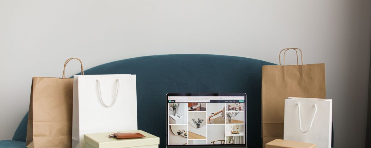 A laptop surrounded by shopping bags and boxes on a blue sofa, ideal for online shopping themes.
