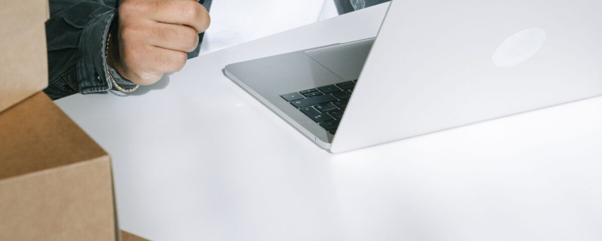 Person using a credit card for online shopping on a laptop surrounded by shipping boxes.