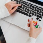Close-up of a person using a laptop and holding a credit card for online shopping.
