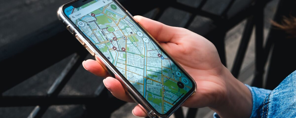 An outdoor close-up of a hand holding a smartphone displaying a map application.