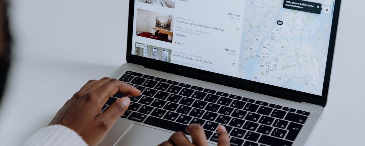 Hands typing on laptop searching Airbnb for accommodation options with map view.